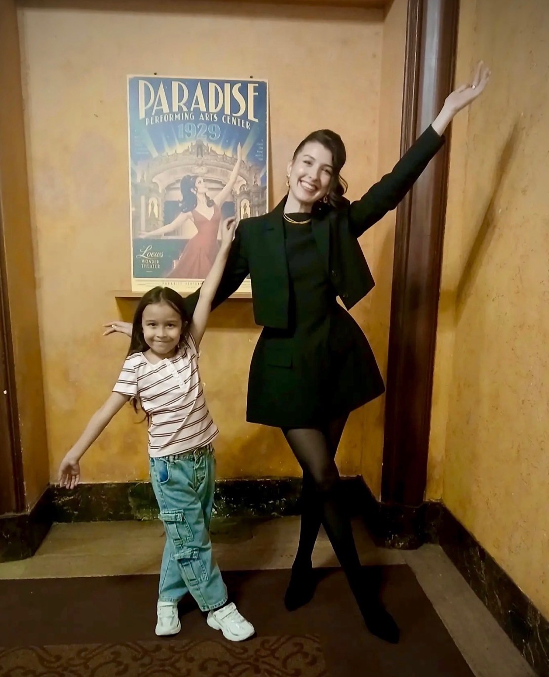 Two visitors pose beside a Paradise Performing Arts Center poster