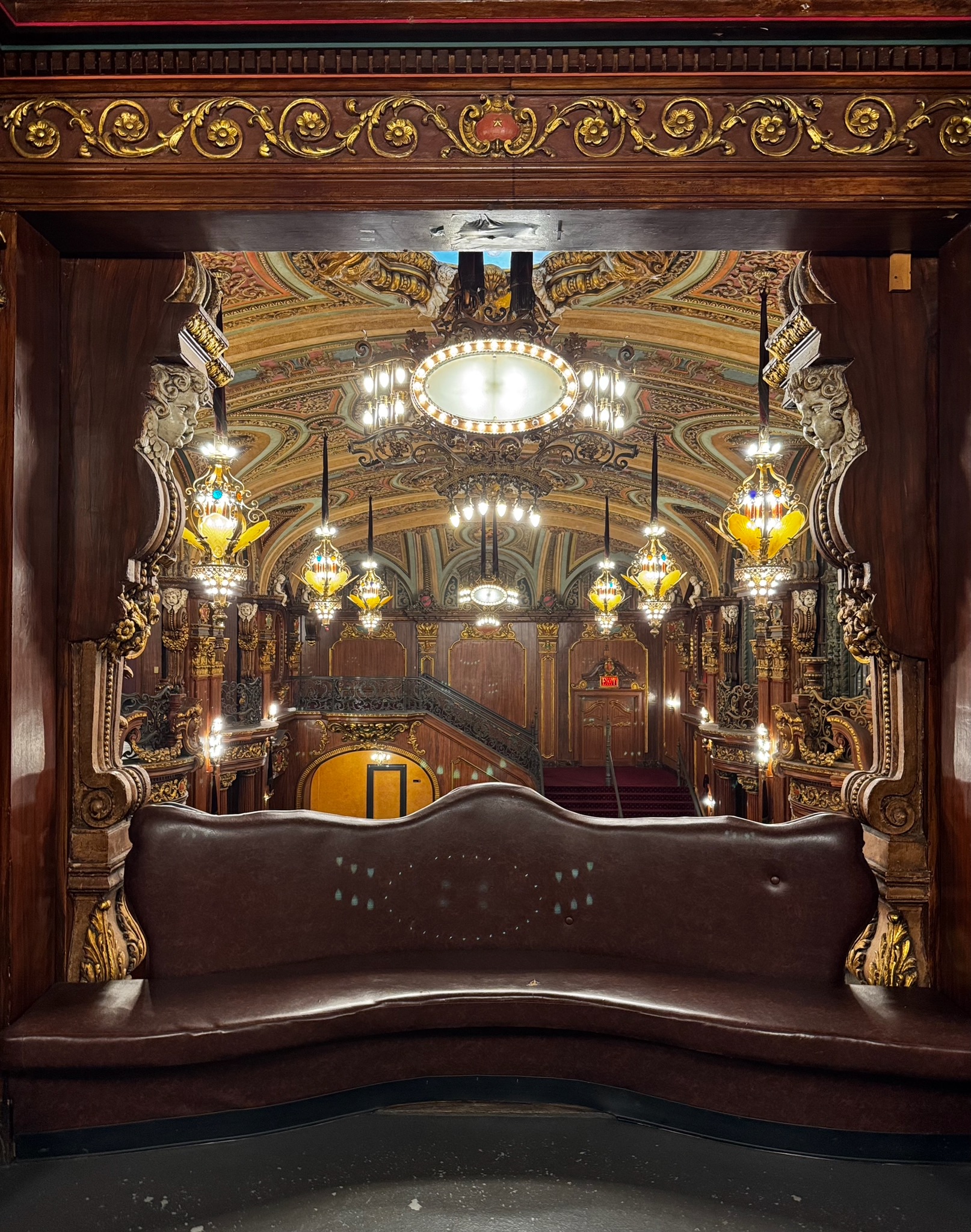 A curved leather bench in the balcony hallway, framed by carved wood and gold ornament, overlooking the Paradise’s illuminated lobby